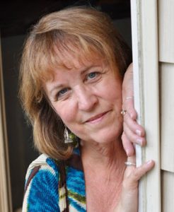 Photo of a woman, the owner of the business, smiling while leaning against a wall.